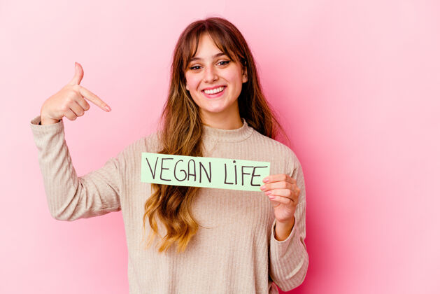 素食者年轻的高加索女子举着素食主义者的生活标语牌孤立的人用手指着一件衬衫的复制空间 骄傲而自信女性指点配料