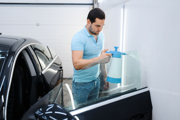 工作男性包装与喷雾准备着色 调整汽车服务工人在车库的车窗上涂乙烯基色 有色汽车玻璃手人车间