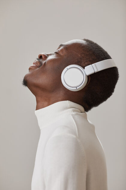 音乐戴着无线耳机的年轻人的侧视图 在灰色的墙上欣赏着与世隔绝的音乐商务侧视图特写