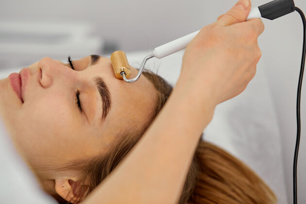 治疗面部按摩用压路机 年轻女子在美容院近距离得到专业医护人员的美容程序病人Spa过程