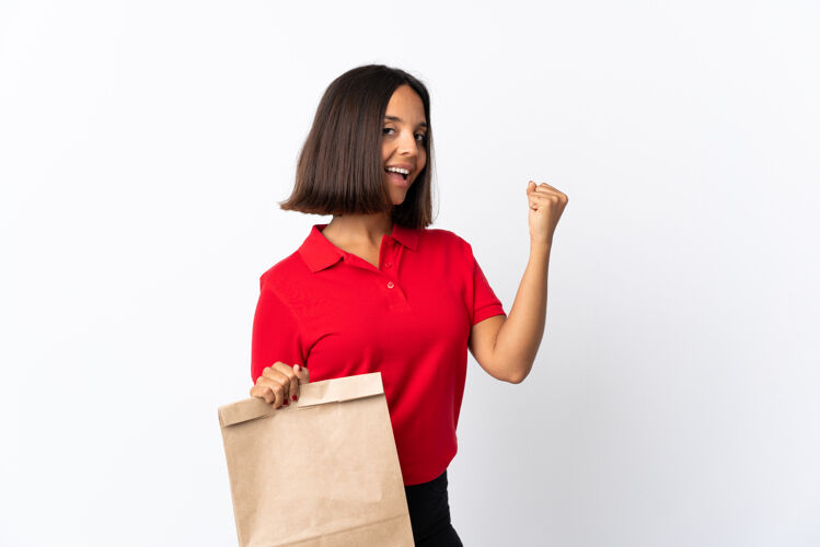 喜悦年轻的拉丁女子拿着一个杂货店购物袋孤立地在白色庆祝胜利权力自豪客户