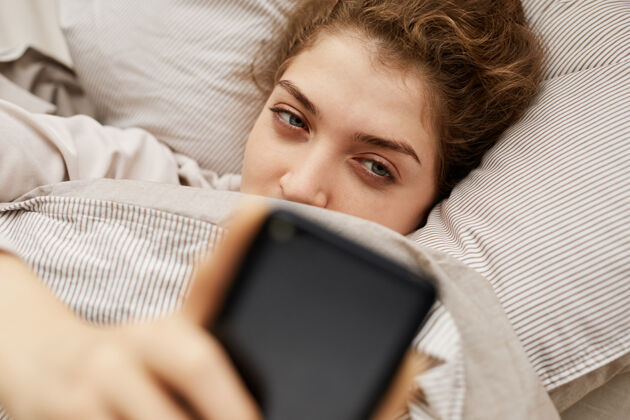 休闲服躺在床上用手机上网聊天的年轻女子抱人看