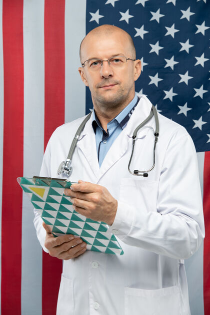 国旗当代中年医生戴着眼镜拿着剪贴板拿着文件 对着相机前的星条旗护理劳工投票