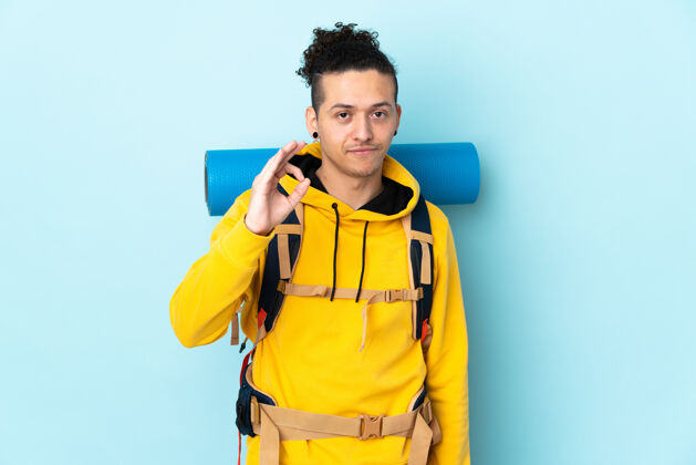 人一个年轻的登山者 背着一个大背包 在孤立的蓝色背景上 用手指画着“ok”的手势Ok旅游拉丁语