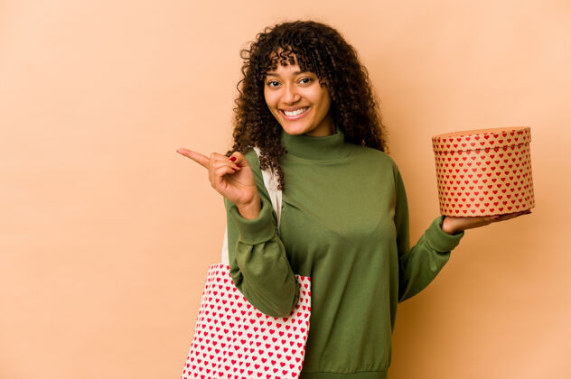红色年轻的非洲裔美国黑人妇女拿着情人节礼物微笑着指着一边 在空白处展示了一些东西心手指情人节