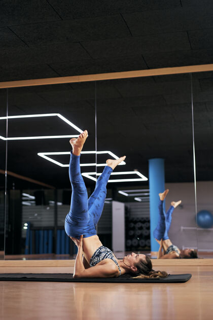 活动体位年轻女子在健身房练习瑜伽或普拉提 穿着蓝色运动服锻炼身体 摆着刀形姿势健身房站立日常生活