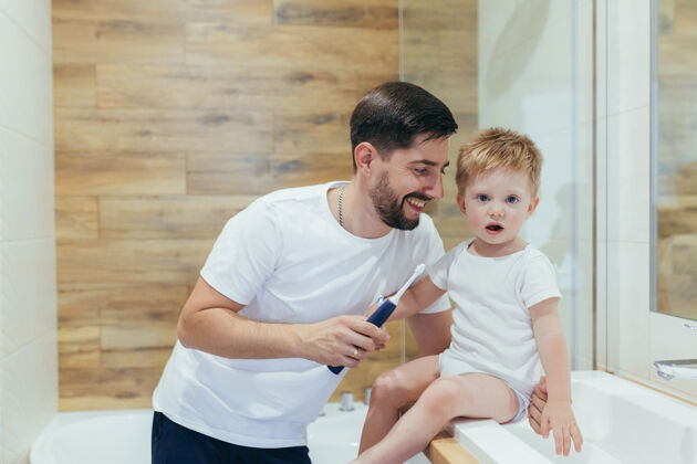 室内老公爸爸教小男孩儿子刷牙单身父亲享受中年