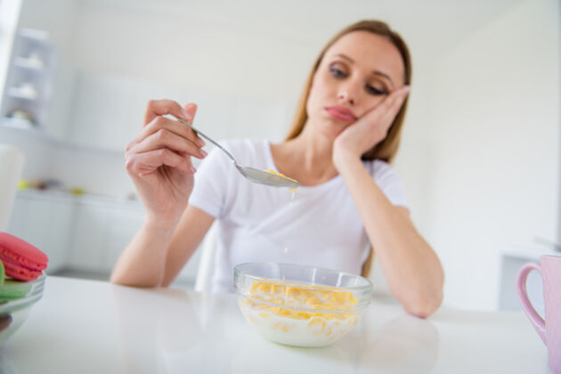 晚餐照片中美丽金发心烦意乱的主妇拿着勺子不想吃牛奶早餐玉米片厌倦节食无聊的餐桌白光厨房室内不开心格兰诺拉麦片零食