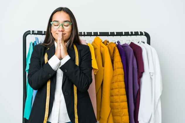 宗教年轻的亚洲女设计师孤零零地站在白色的墙上 手牵着手在嘴边祈祷 感到自信工业亚洲工作