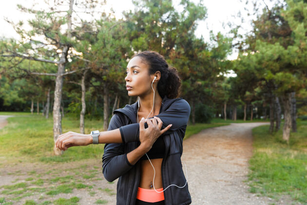 精力充沛一幅20多岁的非洲裔美国妇女穿着黑色运动服在绿色公园锻炼身体的照片运动员非洲听力