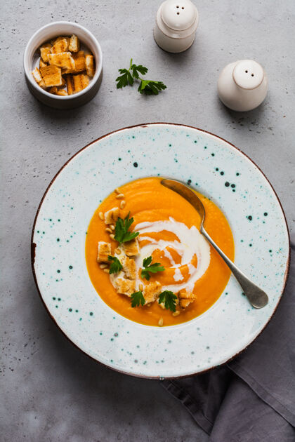 陶瓷奶油南瓜汤 面包片和雪松果仁放在灰色的陶瓷盘子里 放在灰色的桌面上南瓜欧芹顶视图