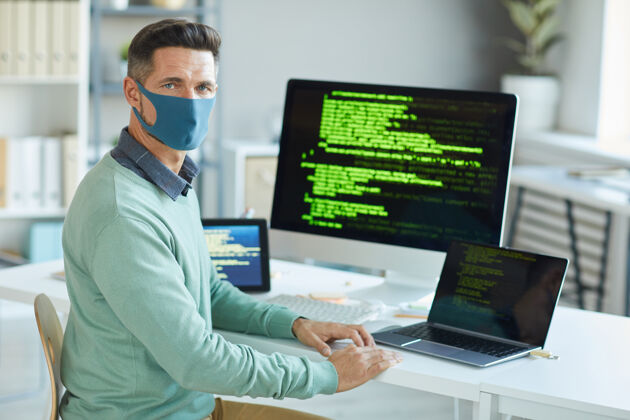 设备戴着防护面具的年轻人在it办公室写代码时注视前方的画像流行病外观技术