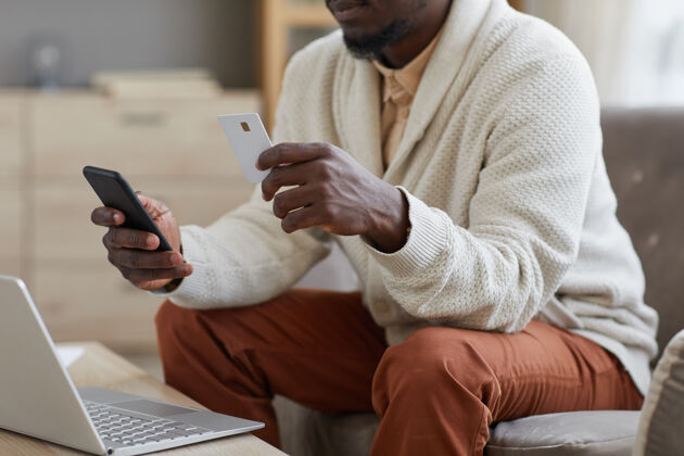 工作商人坐在笔记本电脑前的沙发上用手机和信用卡在线支付的特写镜头在线休闲服电话