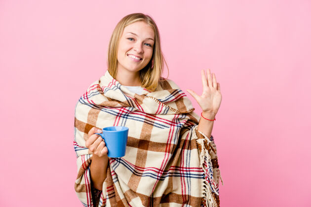 成人年轻的俄罗斯妇女裹着毯子喝着咖啡 微笑着 高兴地用手指指着五号杯子女性添加