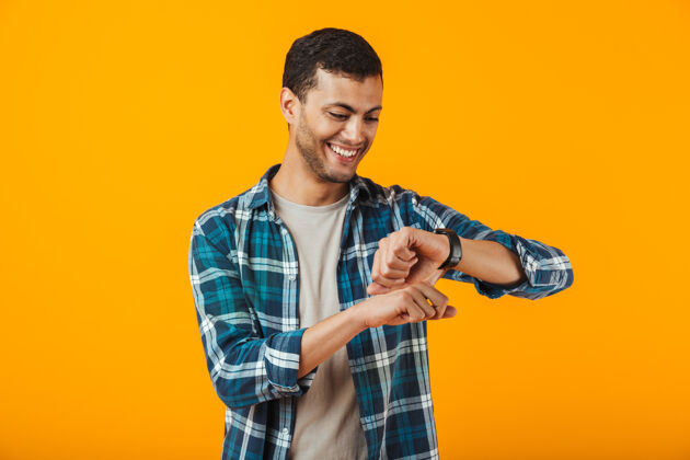 表情一个穿着格子衬衫的年轻人孤零零地站在橙色的墙上 看着他的手表欢呼英俊工作