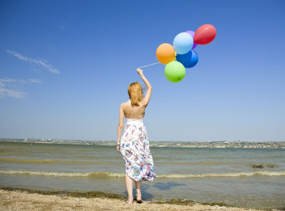 蓝红发女孩带着彩色气球在海边绿水户外