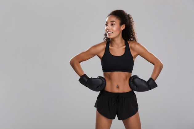 成人一个黑人年轻健美的女运动员在灰色背景下孤立地打拳击 目光转向别处女性强壮吸引力