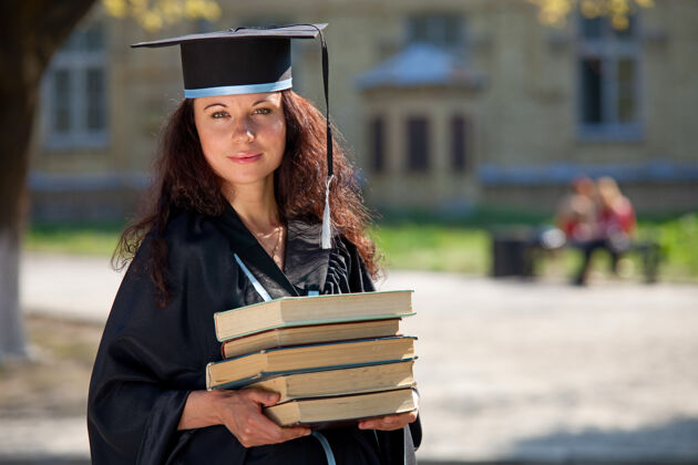 快乐在大学庭院里拿着书的毕业生微笑女人帽子