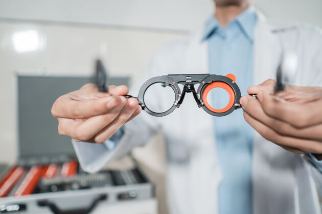 专家一个可调轴试验架是由一个医生在眼科诊所举行的医生背景和一个存储盒亚洲人视力给予
