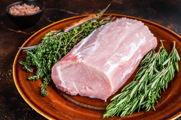 生的新鲜生猪里脊肉配百里香和迷迭香放在乡村盘子里肋骨顶视图肉