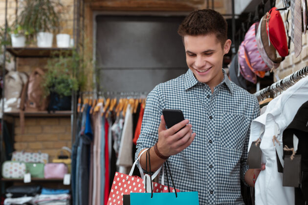 零售阅读信息积极友好的年轻人站在服装店 微笑着用智能手机阅读信息商品腰杆向上顾客