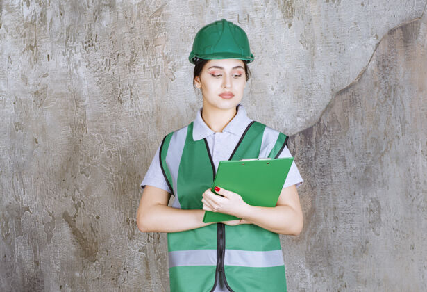 晋升身着绿色制服 头戴安全帽的女工程师拿着项目文件夹建筑师工人报告