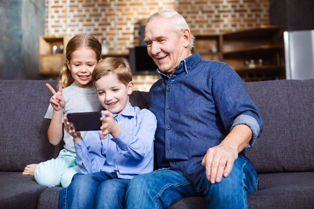 电话积极的退休老人坐在沙发上和孙子孙女们自拍祖父母人孙子