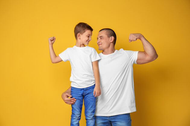 肖像爸爸和他的儿子在彩色墙上展示肌肉秀父亲站立