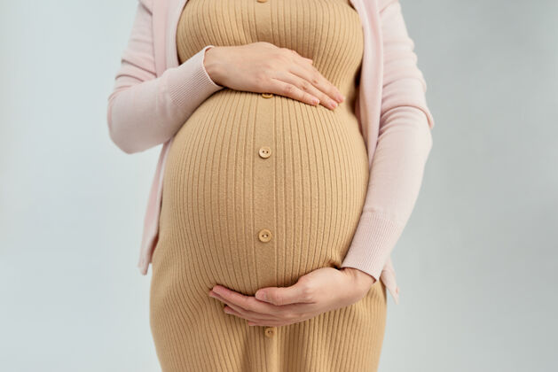 爱怀孕的年轻女子用手抱着她裸露的腹部的正视图美丽母亲肚子