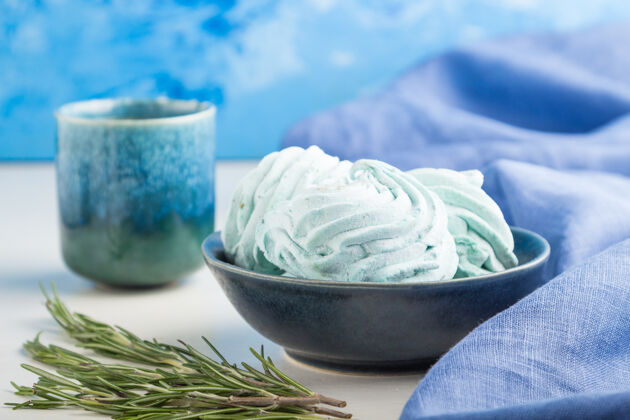 烹饪蓝色的自制西风或棉花糖 在白色木制表面上放一杯咖啡和蓝色纺织品堆杯子俄罗斯