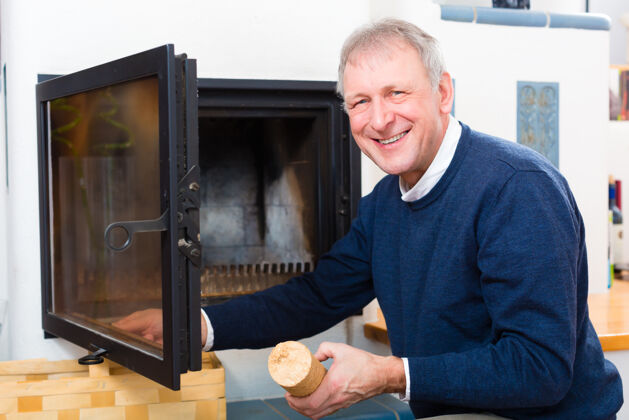 男人生活质量-老人或退休人员在壁炉里生火 他是在家里壁炉房子柴火