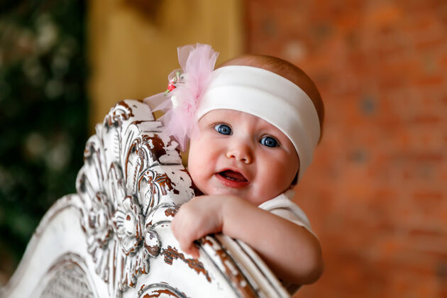 房间可爱快乐的蓝眼睛6个月大的女孩在白色头巾在复古床头年轻女婴儿