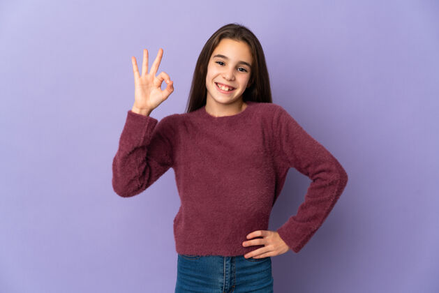 表情被隔离在紫色墙壁上的小女孩用手指显示ok标志自信手认可