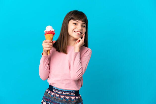 冰淇淋一个拿着短号冰淇淋的小女孩孤零零地站在蓝色的墙上 一边抬头一边想着一个主意冰激凌食物饥饿