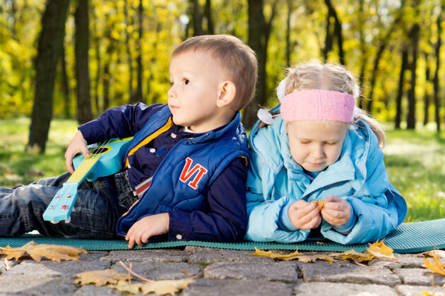 娱乐带着玩具吉他的小女孩和小男孩在公园里享受自由时光年轻一起户外