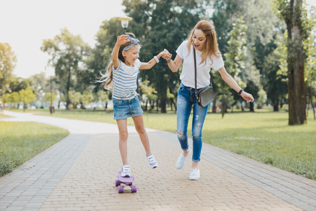 母亲有趣和自由微笑迷人的学龄前女孩感觉有趣和自由 而使用她的滑板养育休息运动