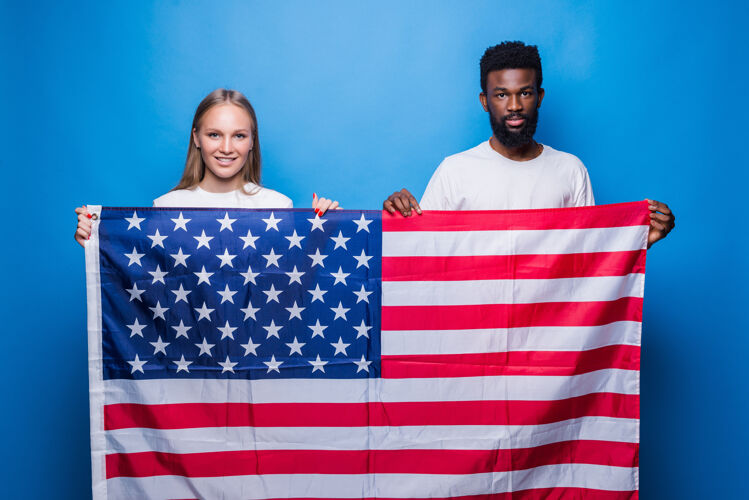 非洲男子一个非洲男人和一个高加索女人在蓝色的墙上举着美国国旗休闲多样性爱国