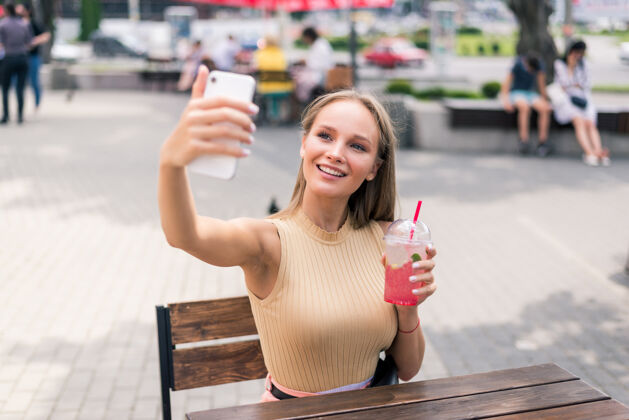 拍摄美丽的年轻女子在夏日街咖啡馆喝着莫吉托自拍人鸡尾酒女人