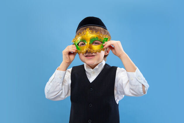 情感戴上狂欢节面具一个年轻的东正教犹太男孩的肖像被隔离在蓝色的墙上光明节犹太面具