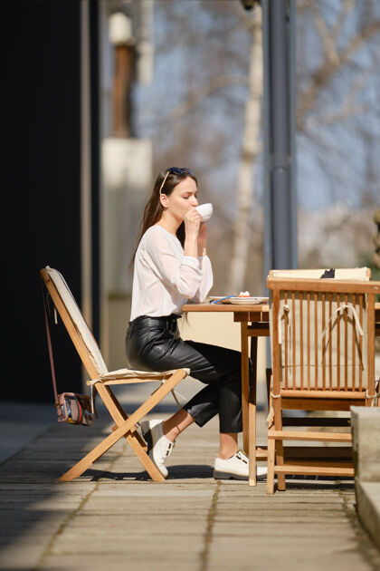 美味阳光明媚的日子里 快乐的年轻女子坐在咖啡馆的露台上喝酒咖啡女人在户外享受春天的第一缕阳光女士肖像年轻