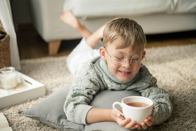 童话一个穿着针织毛衣的漂亮小男孩拿着一杯热咖啡在窗边看书茶舒适秋天秋天的心情聪明小学生沟通