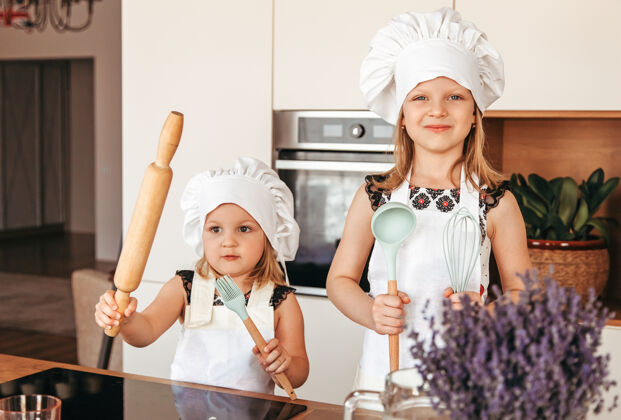 肖像厨房里有两个穿着白围裙和厨师帽的小女孩女孩面包房子