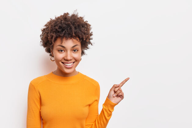 决定美丽的卷发非裔美国妇女建议点击链接点在空白的复制空间显示方式站在白墙穿基本的橙色套头衫人和广告的概念高兴非洲脸