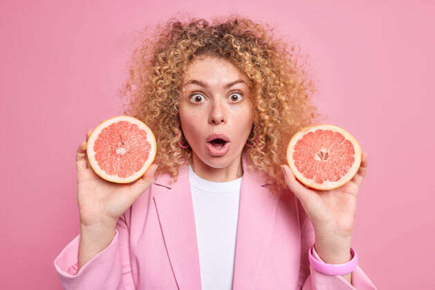 奇迹令人印象深刻的欧洲女人拿着两半新鲜的葡萄柚惊讶地发现了有用的物质 这种柑橘类水果含有卷发隔离粉红色的墙壁节食时尚夹克脸