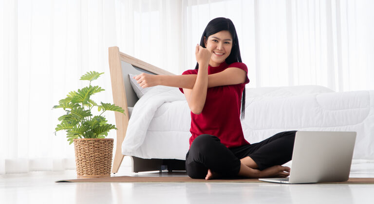 锻炼健康的亚洲年轻女子坐在卧室里练习瑜伽 在家里用笔记本电脑在线学习房子运动健康