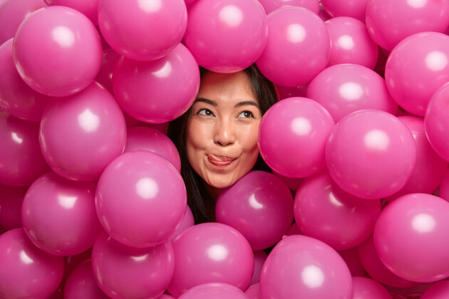 乐趣女人舔着嘴唇 舌头集中在上面 沉思地被充气的粉色气球包围着可爱个人黑发