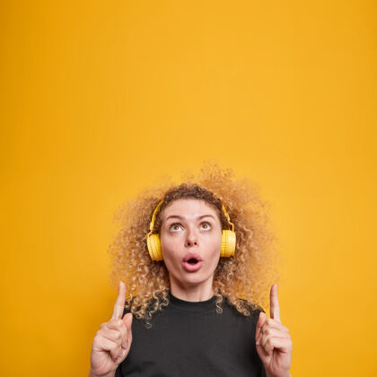 奇迹上面是一个奇怪的年轻女子 头发卷曲 戴着耳机听音乐 穿着休闲的黄色t恤 隔着黄色的墙旋律歌曲室内