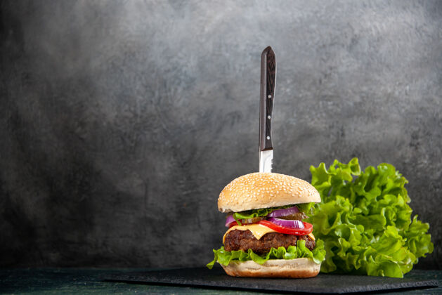 芝士汉堡刀在美味的三明治和绿色的黑色托盘上的左侧半暗浅色表面与自由空间刀左边美味