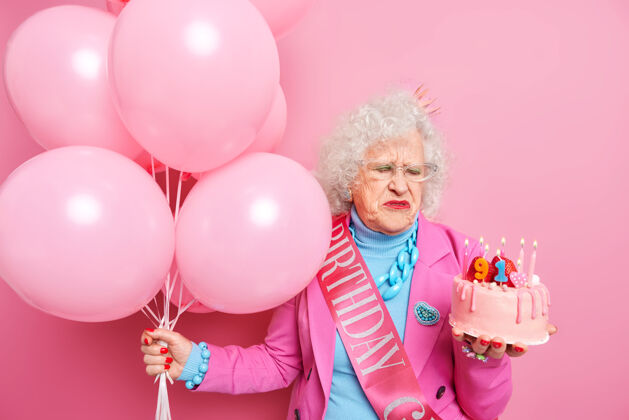老年人不开心的老美女伤心变老看着燃烧着蜡烛的美味蛋糕庆祝91岁生日霍尔兹一堆气球接受派对的祝贺老化概念事件欧洲聚会