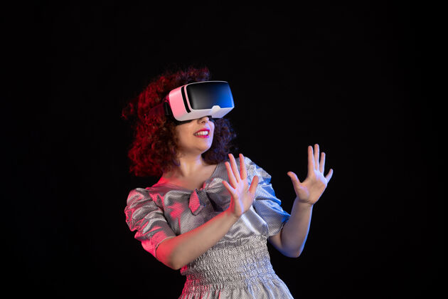 穿着年轻女性戴着虚拟现实耳机在黑暗的桌面上玩视觉游戏技术视觉年轻女性现实